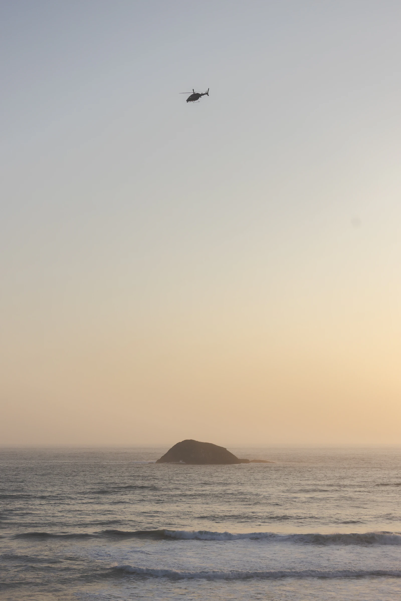 Helicóptero sobrevolando el océano al atardecer